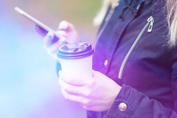 Una chica está caminando por la mañana en un parque con un teléfono inteligente y café, tonificación ligera — Foto de Stock