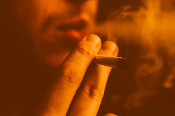 A joint in hand A man smokes cannabis weed, . Smoke on a black Yellow toning — Stock Photo, Image