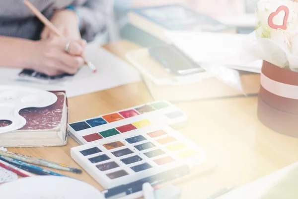 Mujer joven bastante sonriente dibujando un cuadro con pintura de póster. Vista frontal en chica de dibujo con paleta en la mano. Mujer joven sonriente dibujar un cuadro en el estudio, tonificación de la luz — Foto de Stock