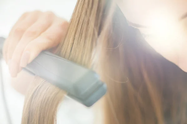 Γυναίκα κάνει χτένισμα με το ίσιωμα των μαλλιών, φως τόνωση — Φωτογραφία Αρχείου