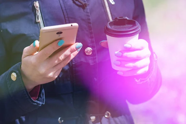 Una chica está caminando por la mañana en un parque con un teléfono inteligente y café, tonificación ligera — Foto de Stock