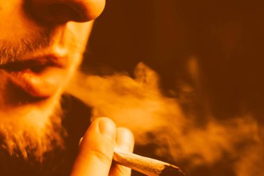 adam elinde ortak. Bir adam esrar ot çekiyor bir. Bir sarı tonlama duman