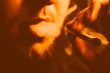 Siyah bir arka plan üzerinde duman. Bir adam bir ortak sarı tonlama esrar ot çekiyor