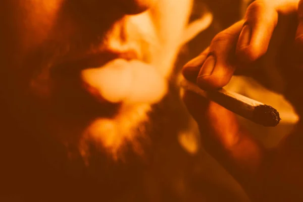 Rauch auf schwarzem Hintergrund. ein Mann raucht Cannabiskraut, einen Joint mit gelber Tonung — Stockfoto