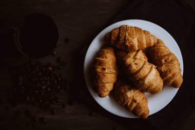 Makro vurdu. Kahvaltı kavramı. Tatlı ve kahve. Moody renk dostum. Siyah bir zemin üzerine taze kruvasan ve kahve üstten görünüm.