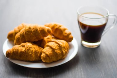 Moody renk dostum. Yakın çekim. Amerikan kahve ve siyah bir zemin üzerine taze kruvasanlar. Kahvaltı kavramı. Tatlı ve kahve.