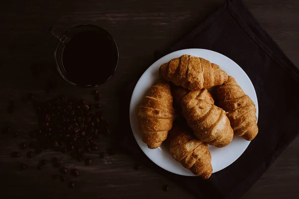 Frühstückskonzept. Dessert und Kaffeebohnen. Ansicht von oben. Makroaufnahme von frischen Croissants und Kaffee auf schwarzem Hintergrund. Mate launische Farbe. — Stockfoto