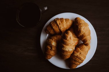 taze kruvasan ve kahve siyah bir arka plan. Kahvaltı kavramı. Tatlı ve kahve. Makro vurdu. Dostum moody renk.