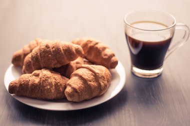 Amerikan kahve ve siyah bir zemin üzerine taze kruvasanlar. Kahvaltı kavramı. Tatlı ve kahve. Dostum moody renk