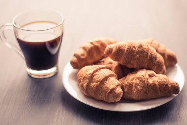 Tatlı ve kahve. Moody renk dostum. Yakın çekim. Amerikan kahve ve siyah bir zemin üzerine taze kruvasanlar. Kahvaltı kavramı.