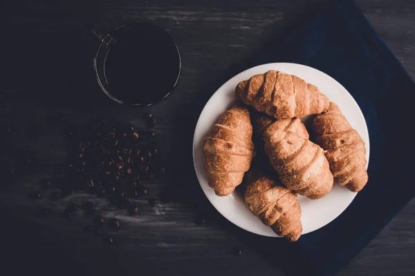 Concept of breakfast. Dessert and coffee beans. Top view. Macro shot of fresh croissants and coffee on a black background. Mate moody color. — Stock Photo, Image