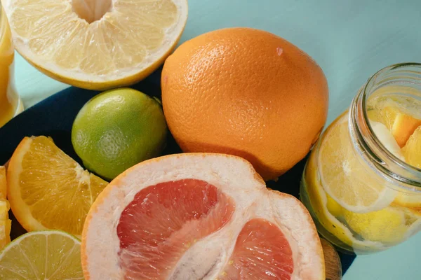 Cítricos, naranjas, limones, limas, pomelo sobre tabla vintage, limonada y zumo en un vaso de vidrio sobre fondo turquesa — Foto de Stock