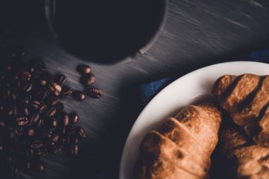 Moody renk dostum. Kahvaltı kavramı. Üstten görünüm. Makro çekim taze kruvasan ve kahve siyah bir arka plan. Tatlı ve kahve çekirdekleri.