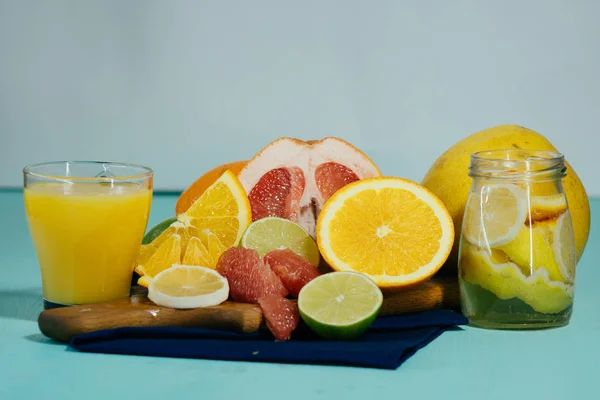 Citrus, oranges, lemons, limes, grapefruit, pomelo on vintage board, lemonade and juice in a glass of glass on a turquoise background