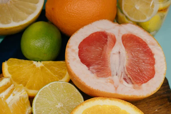Agrumes, oranges, citrons, limes, pamplemousse, pomelo sur carton vintage, limonade et jus dans un verre sur fond turquoise — Photo