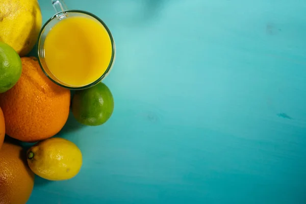 Fruta de cítricos, naranja, lima, limón, pomelo, pomelo con zumo de naranja en un vaso de vidrio. Espacio para la firma en segundo plano — Foto de Stock