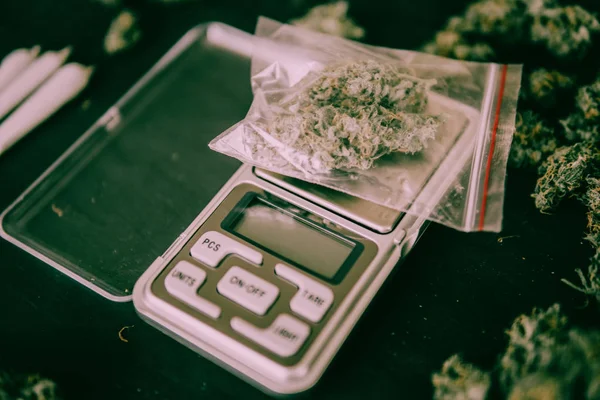 Paquete de Marihuana En las escalas Brotes de cannabis en el paquete sobre la mesa y articulación sobre la mesa en un tono verde malhumorado — Foto de Stock