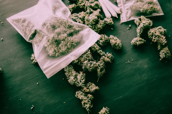 Brotes de cannabis en el paquete en la mesa y articulación en la mesa en un tono verde malhumorado — Foto de Stock
