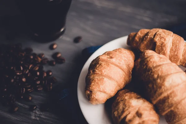 Desszert és szemes kávé. Mate moody színe. A koncepció a reggeli. Makro szemcsésedik-ból friss croissant és kávé a fekete háttér. — Stock Fotó