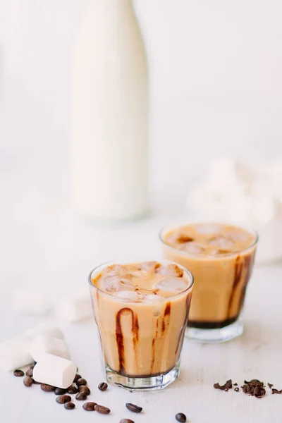 Disparo vertical. Fondo claro. Café helado. Concepto de bebida refrescante. Marshmelow y granos de café en la mesa. Bebida de verano. Café frío con leche y chocolate . — Foto de Stock