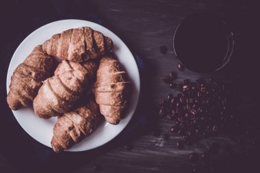 Moody renk dostum. Üstten görünüm. taze kruvasan ve kahve siyah bir arka plan. Makro vurdu. Kahvaltı kavramı. Tatlı ve kahve.