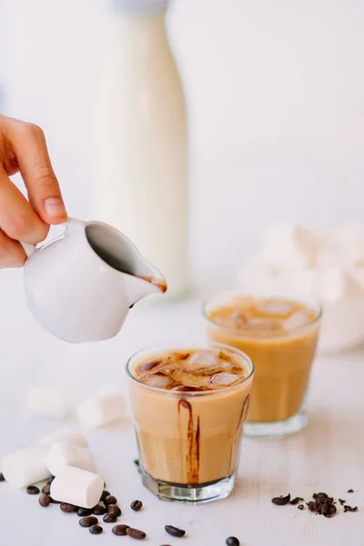 Light background. Iced coffee. Concept of a cooling drink. Marshmelow and coffee beans on the table. Summer drink. Cold coffee with milk and chocolate.