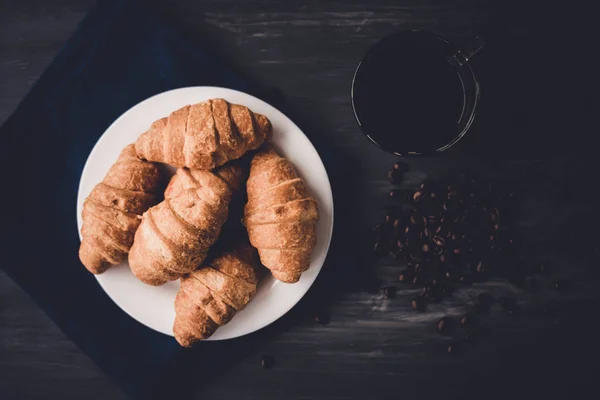 Frühstückskonzept. Dessert und Kaffeebohnen. Ansicht von oben. Makroaufnahme von frischen Croissants und Kaffee auf schwarzem Hintergrund. Mate launische Farbe. — Stockfoto