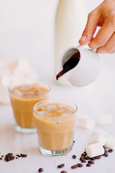 Café helado. Concepto de bebida refrescante. Marshmelow y granos de café en la mesa. Bebida de verano. Café frío con leche y chocolate. Fondo claro . — Foto de Stock