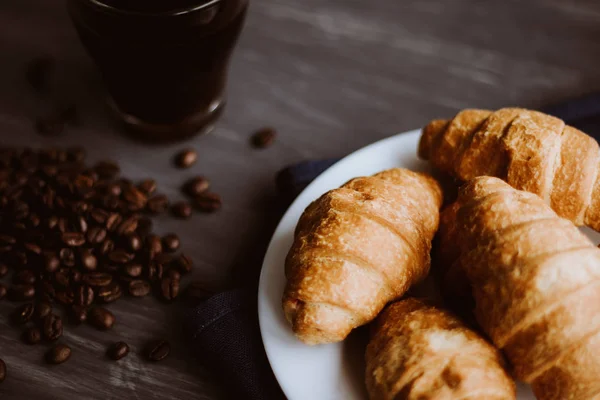 Das Konzept des Frühstücks. Makroaufnahme von frischen Croissants und Kaffee auf schwarzem Hintergrund. Dessert und Kaffeebohnen. Mate launische Farbe. — Stockfoto