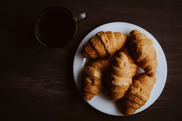 A koncepció a reggeli. Makro lövés. Mate moody színe. friss croissant és kávé a fekete háttér. Desszert és kávé. — Stock Fotó