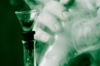 Sigara esrar otu, nargile ve onun elinde bir çakmak bong. Siyah bir arka plan üzerinde duman. Tıbbi esrar kullanım ve yasallaştırma esrar kavramları. Siyah bir arka plan üzerinde yeşil renklendirme