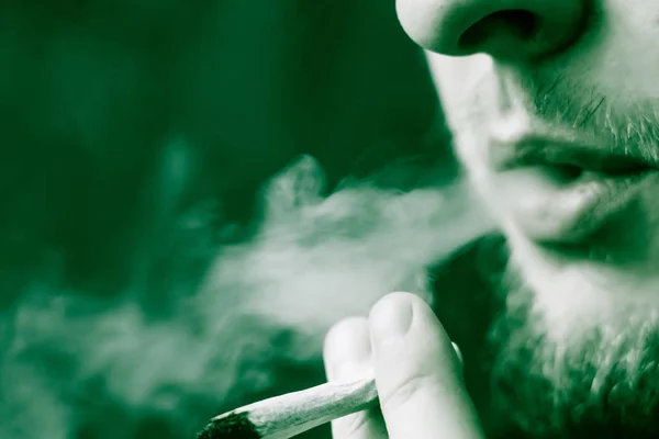 Konopí trávu, spoj ve své ruce A muž kouří. Kouř na černém pozadí. Koncepce užívání lékařské marihuany a legalizace konopí. Na černém pozadí zelené tónovací — Stock fotografie
