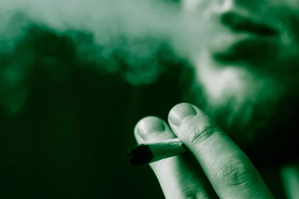 Człowiek pali cannabis weed, wspólne i lżejsze w jego ręce. Pali na czarnym tle. Pojęcia dotyczące używania marihuany i legalizacji konopi. Na czarnym tle zielony barwienia — Zdjęcie stockowe