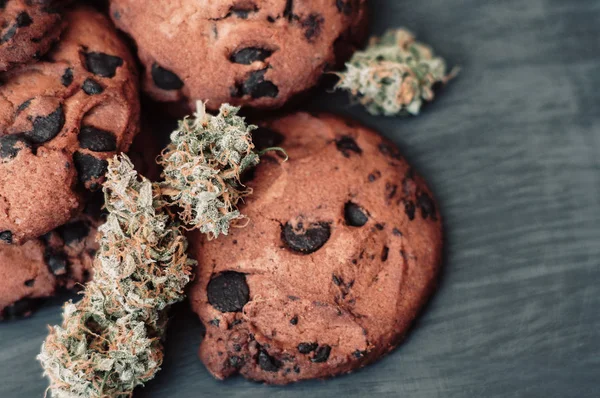 Sweets with weed. Chocolate cookies with marijuana. Sweets with cannabis. Cannabis buds on a black background. Baking with the addition of CBD. top view — Stock Photo, Image
