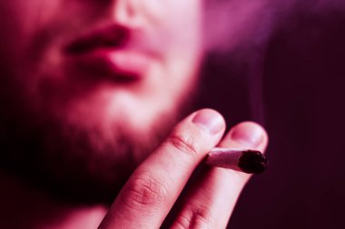 Esrar, elinde esrar Bir adam sigara içiyor. Siyah arka planda sigara içmek. Tıbbi marihuana kullanımı ve esrar kullanımının yasallaştırılması kavramları. Siyah bir arkaplanda Violet boyası