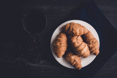 Üstten görünüm. Makro çekim taze kruvasan ve kahve siyah bir arka plan. Moody renk dostum. Kahvaltı kavramı. Tatlı ve kahve çekirdekleri.