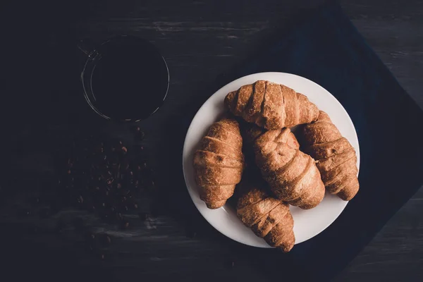 Top view. Macro shot of fresh croissants and coffee on a black background. Mate moody color. concept of breakfast. Dessert and coffee beans. — Stock Photo, Image