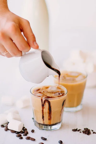 Light background. Iced coffee. Concept of a cooling drink. Marshmelow and coffee beans on the table. Summer drink. Cold coffee with milk and chocolate.