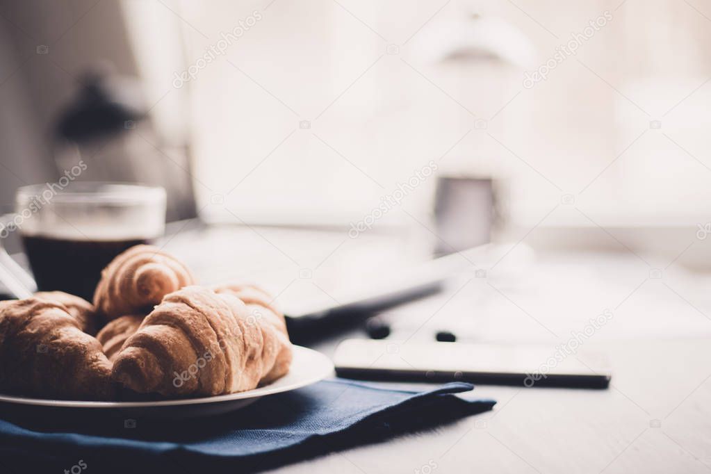 concept of work. Macro shot of Smartphone and Laptop fresh croissants and coffee black background. Mate moody color.
