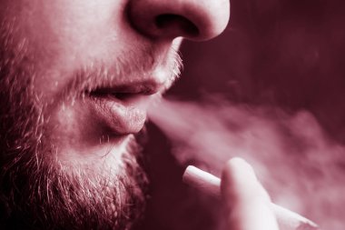 Bir adam elinde esrar, esrar ve çakmak tüttürür. Siyah arka planda sigara içmek. Tıbbi marihuana kullanımı ve esrar kullanımının yasallaştırılması kavramları. Siyah bir arkaplanda Violet boyası