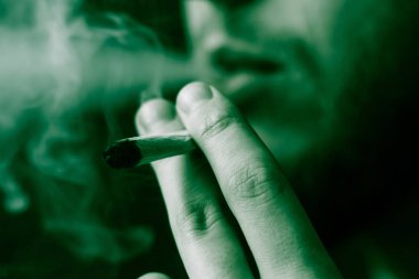 Tıbbi esrar kullanım ve yasallaştırma esrar kavramları. Siyah bir arka plan üzerinde duman. Bir adam sigara esrar esrar, esrar ve çakmak elinde. Siyah bir arka plan üzerinde yeşil renklendirme