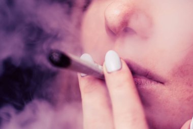 esrar otu A kadın sigara, bir ortak ve bir çakmak onun elinde. Siyah bir arka plan üzerinde duman. Tıbbi esrar kullanım ve yasallaştırma esrar kavramları. Pembe siyah bir arka plan renklendirme