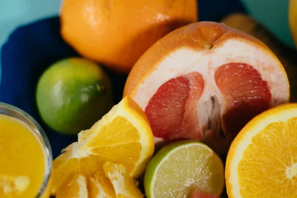 Cítricos, naranjas, limones, limas, pomelo sobre tabla vintage, limonada y zumo en un vaso de vidrio sobre fondo turquesa — Foto de Stock