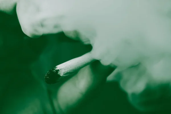 大麻杂草一个人抽烟, 一个关节和他手中的打火机。黑色背景下的烟雾。医疗用大麻的概念和大麻的合法化。在黑色背景绿色着色 — 图库照片