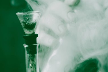 Sigara ve esrar otu, nargile ve onun elinde bir çakmak. Siyah bir arka plan üzerinde duman. Tıbbi esrar kullanım ve yasallaştırma esrar kavramları. Siyah bir arka plan üzerinde yeşil renklendirme