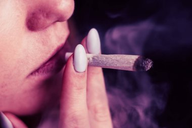 Esrar, elinde esrar Bir kadın sigara içiyor. Siyah arka planda sigara içmek. Tıbbi marihuana kullanımı ve esrar kullanımının yasallaştırılması kavramları. Siyah arka planda Pembe renklendirme