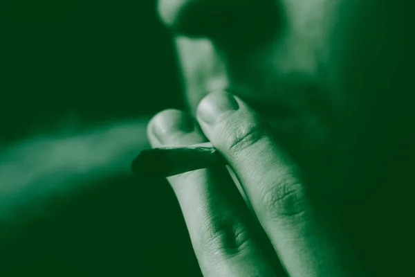 Smokes weed cannabis, A man joint in his hands. Smoke on a black background. Concepts of medical marijuana use and legalization of the cannabis. On a black background Green Tinting — Stock Photo, Image