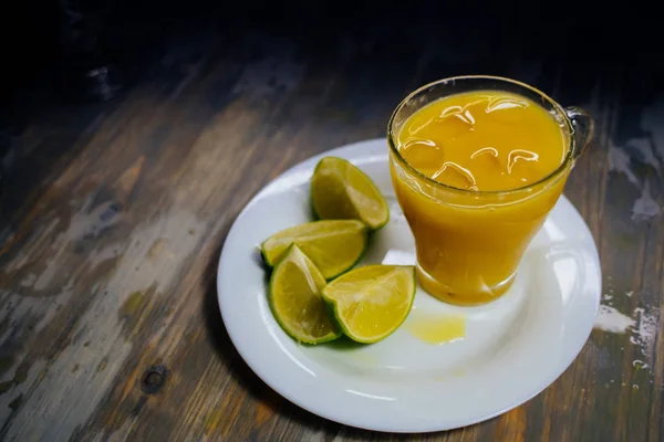 Een glas sinaasappelsap met een grote plons en kalk op een plaat — Stockfoto