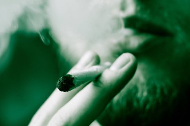 Sigara ve esrar esrar, esrar ve onun elinde bir çakmak. Siyah bir arka plan üzerinde duman. Tıbbi esrar kullanım ve yasallaştırma esrar kavramları. Siyah bir arka plan üzerinde yeşil renklendirme