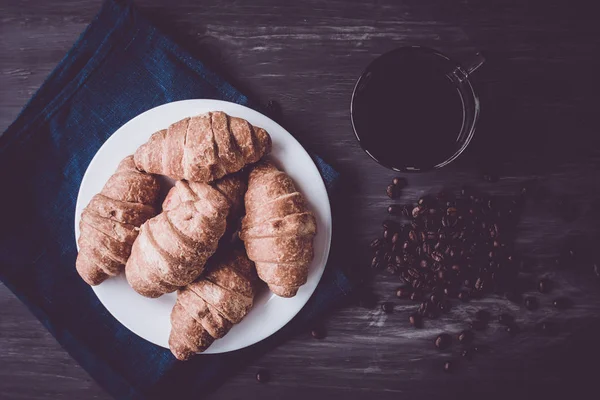 Dessert und Kaffeebohnen. Ansicht von oben. Makroaufnahme von frischen Croissants und Kaffee auf schwarzem Hintergrund. Mate launische Farbe. Frühstückskonzept. — Stockfoto